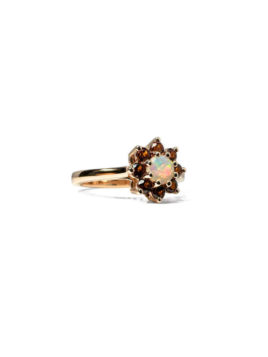 Rose gold engagement ring with a crystal opal at the center and 8 brown gemstones surrounding it in a flower pattern